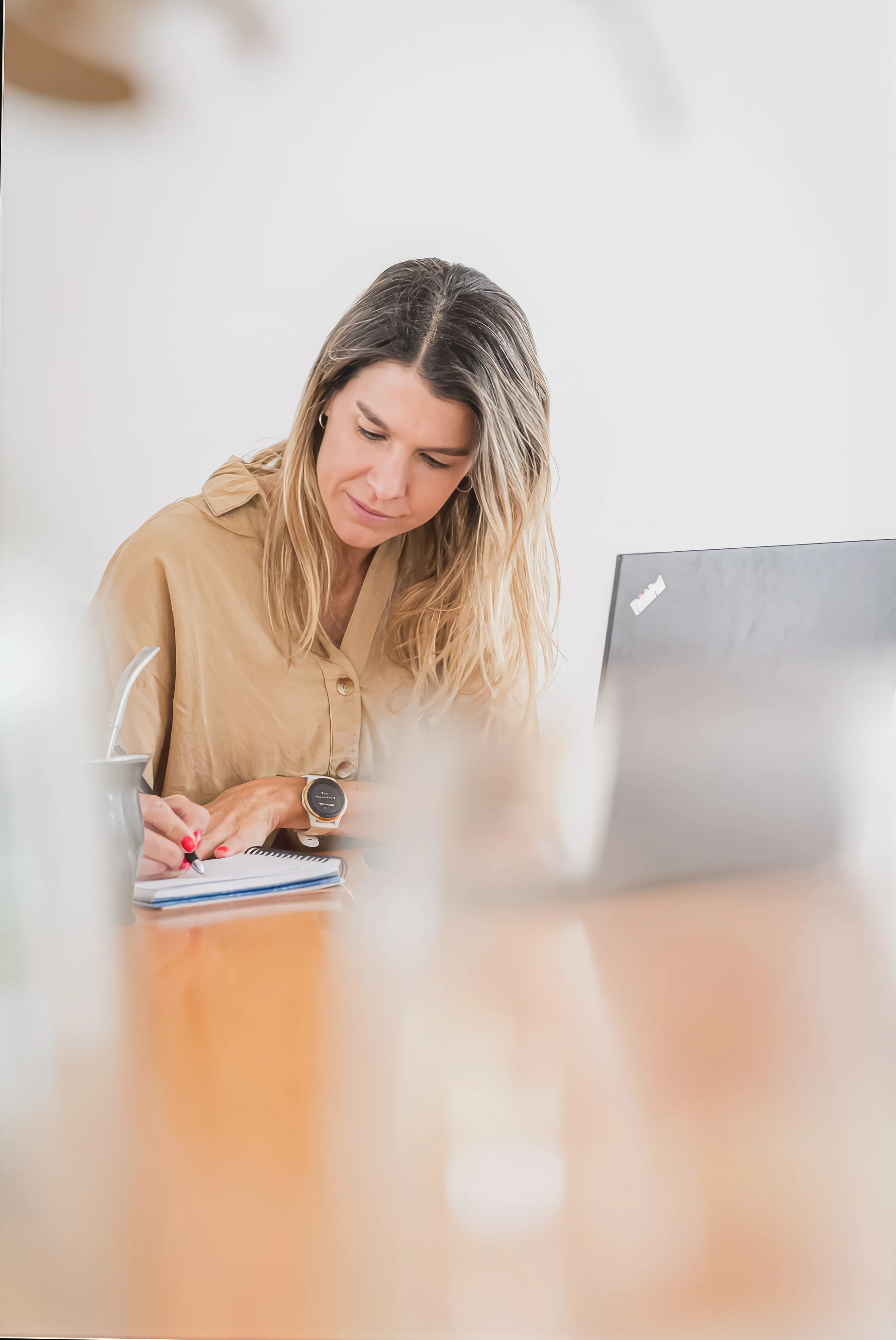Natalia Goñi con camisa beige, escribiendo en un cuaderno frente a su notebook, con un mate en la mesa